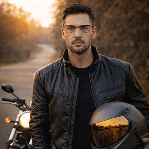Man in a leather jacket holding a helmet with a motorcycle in the background