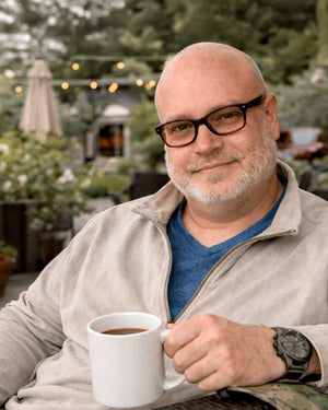 Man with glasses holding a coffee mug outdoors