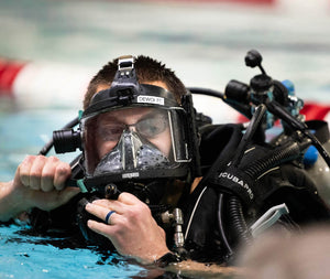 Person wearing scuba diving gear with a mask and equipment underwater.